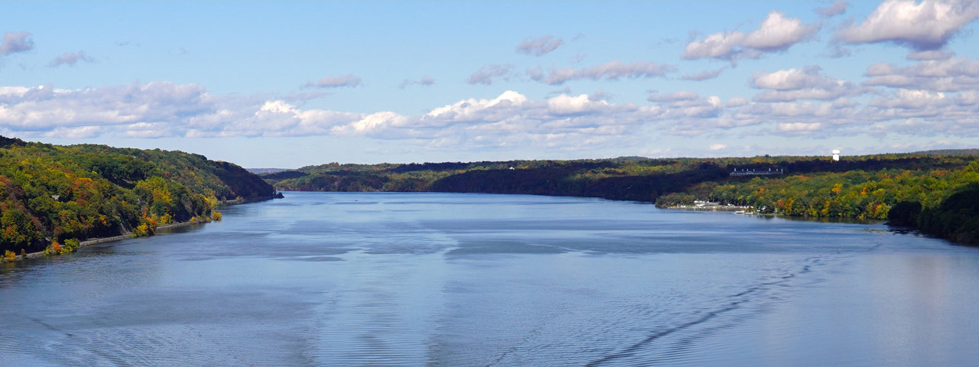 Wide river landscape with green hills and a clear blue sky.